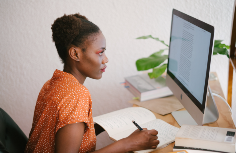 An african american girl taking notes in front of a computer