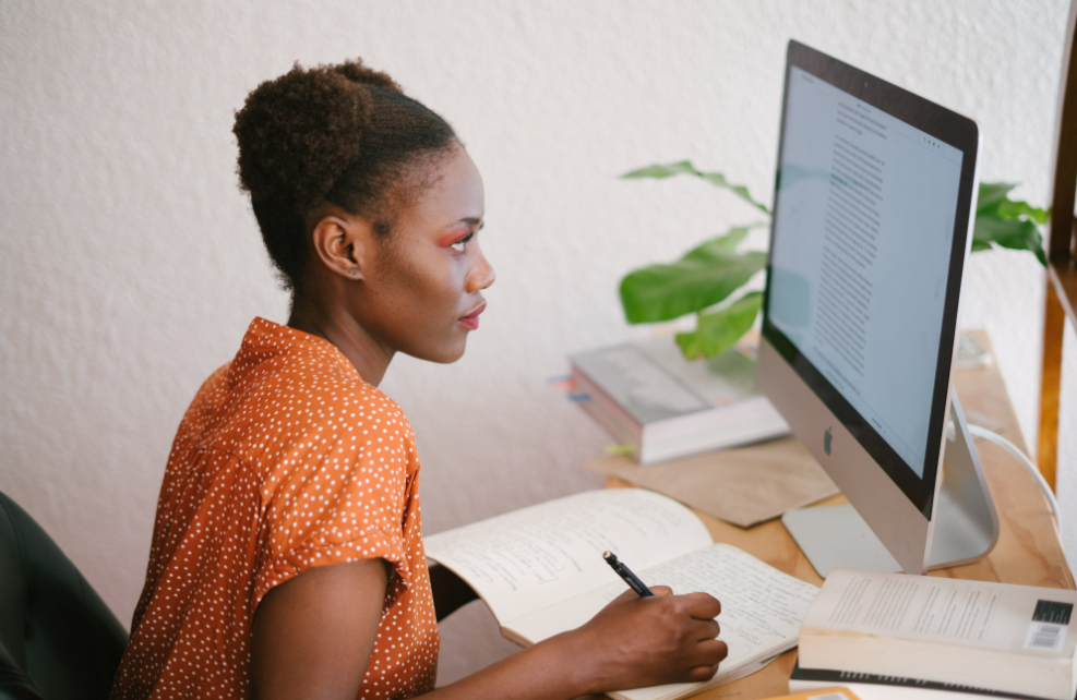 An african american girl taking notes in front of a computer